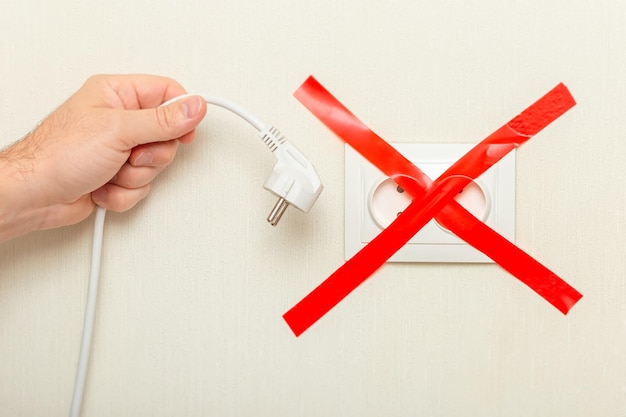 Photo a hand holds a drooping cord with a plug near an electrical outlet tied with a ribbon crosswise