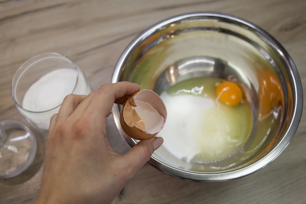 手は砂糖と卵のボウルの背景に卵殻を保持します