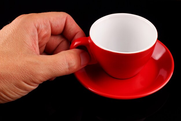 The hand holds an empty red cup and a saucer on a black surface