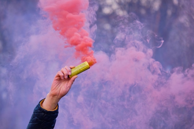 The hand holds a fireworks with a smoke of the color of pink.