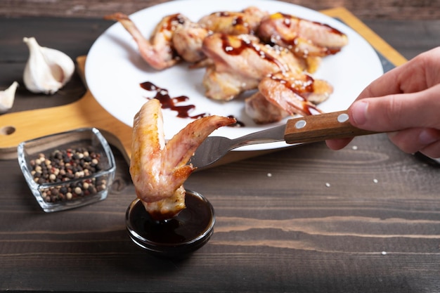 The hand holds the fork with the chicken wing and dips it in the teriyaki sauce Dish of Asian cuisine