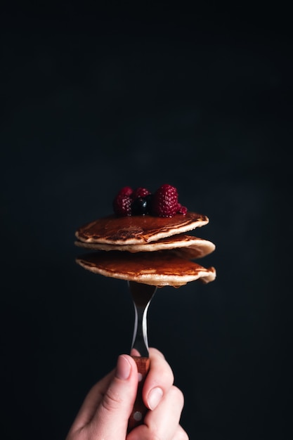 La mano tiene una forchetta con frittelle succose con frutti di bosco e miele. foto di alta qualità