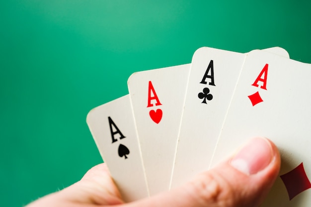 Hand holds four aces on a green background.