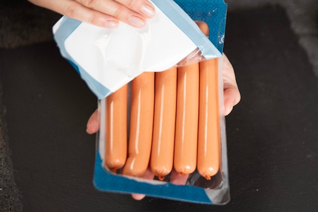 A hand holds fresh sausages from a pack closeup the process of cooking sausages