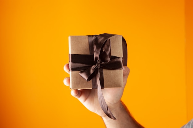 Hand holds gift box on orange background