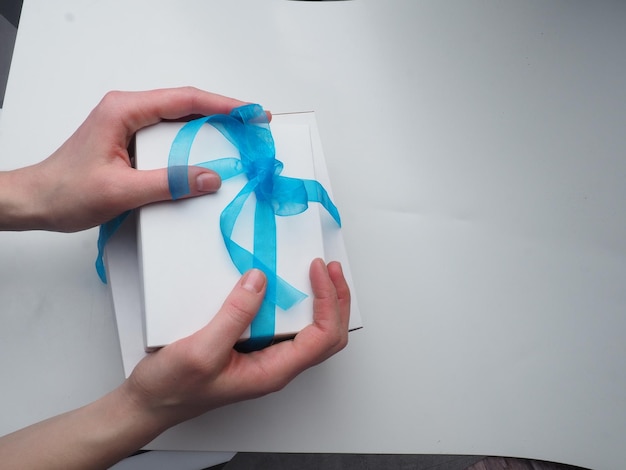 A hand holds a gift box with a blue bow.
