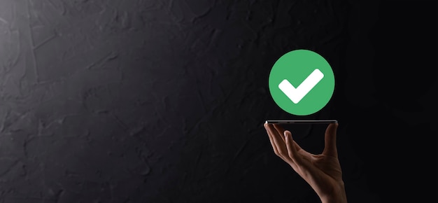 Hand holds green icon Check mark,Check Mark Sign, Tick Icon,right sign,circle green checkmark button,Done.On dark background.Banner.Copy space.Place for text.