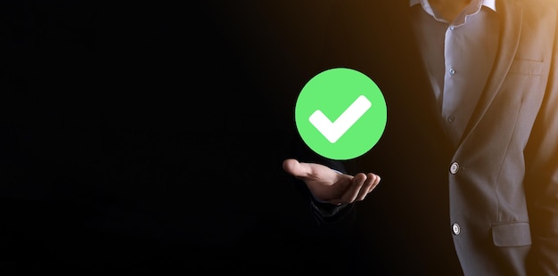 Hand holds green icon check mark,check mark sign, tick\
icon,right sign,circle green checkmark button,done.on dark\
background.banner.copy space.place for text.