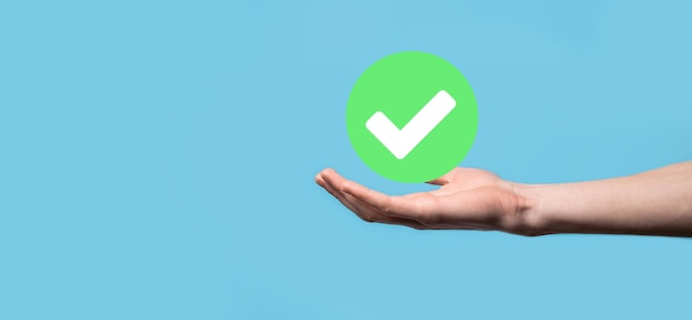 Hand holds green icon check mark,check mark sign, tick\
icon,right sign,circle green checkmark button,done.on dark\
background.banner.copy space.place for text.