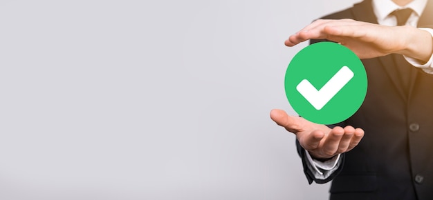 Hand holds green icon check mark,check mark sign, tick\
icon,right sign,circle green checkmark button,done.on grey\
background.banner.copy space.place for text.