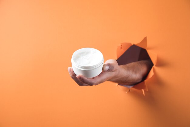 Hand holds hand cream on orange background