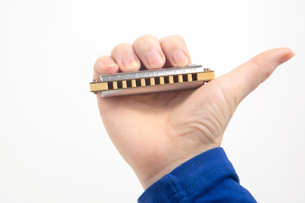 The hand holds a harmonica on a white background. Classical musical wind instrument