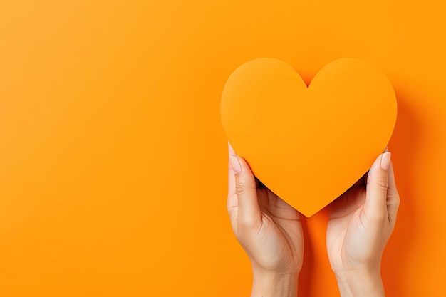 Hand holds a heart love shape on an orange background with copy space