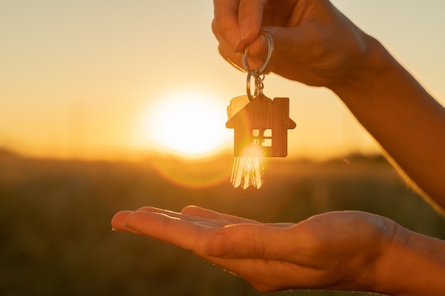 The hand holds the key to the new house with a keychain in the form of a house on the background of ...