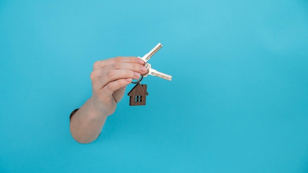 Hand holds the keys with a keychain in the shape of a house on a blue background widescreen