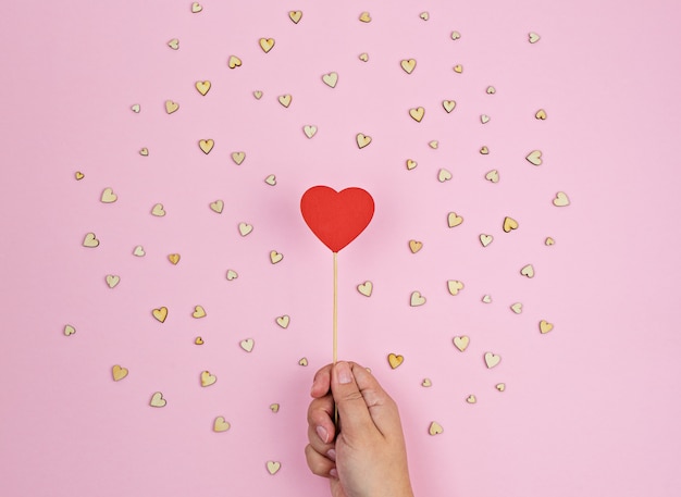 Hand holds large red wooden heart on pink background