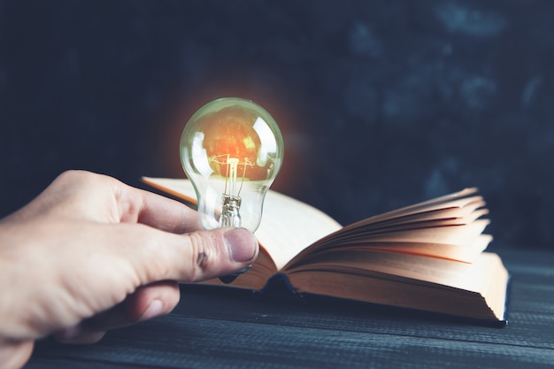 Hand holds a light bulb next to a book