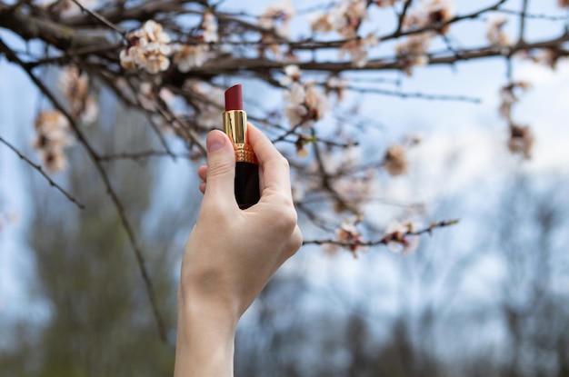 Hand holds lipstick on the background of blossoming tree