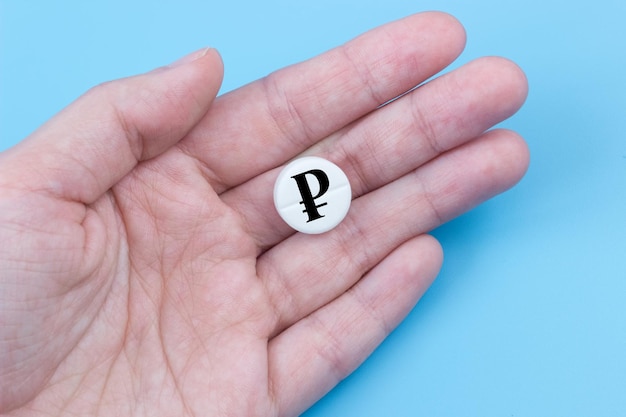 A hand holds a medical pill with a ruble currency sign on a blue background The concept of a rise in the price of medicines in Russia Pharmaceutical business