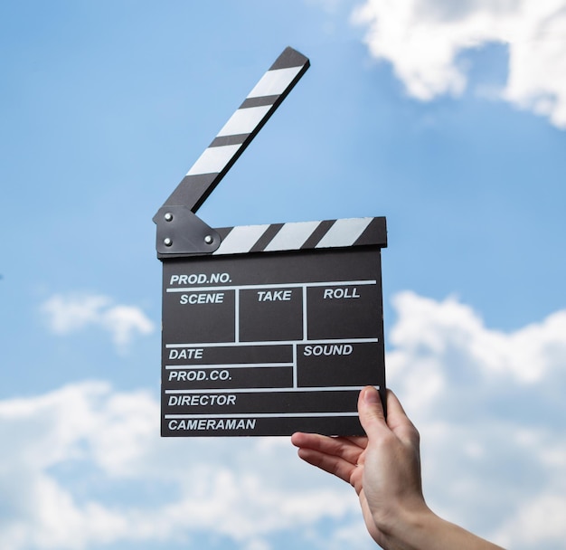 Hand holds movie board on background of blue sky with clouds