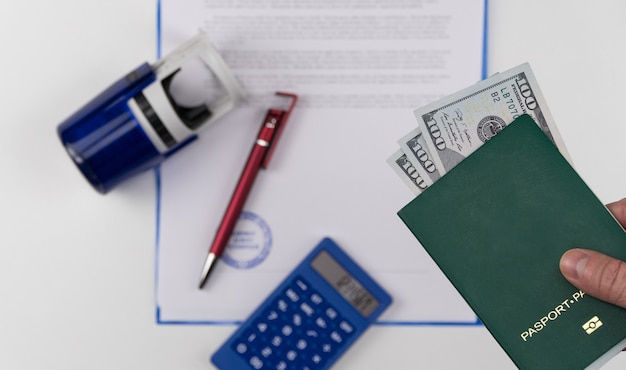 Hand holds out the green passport with US dollars on the background of documents and rubber stamp