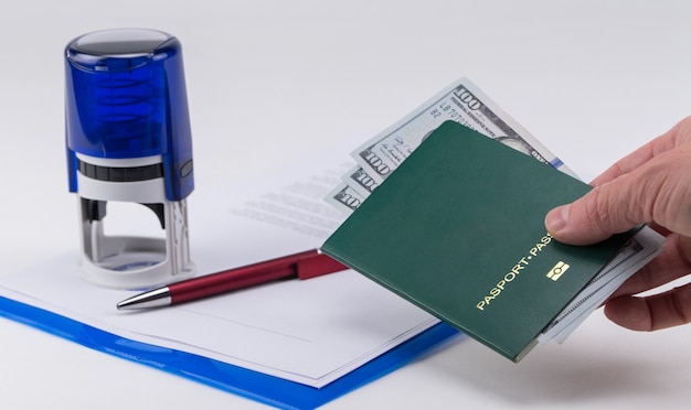 Hand holds out the green passport with US dollars on the background of documents and rubber stamp