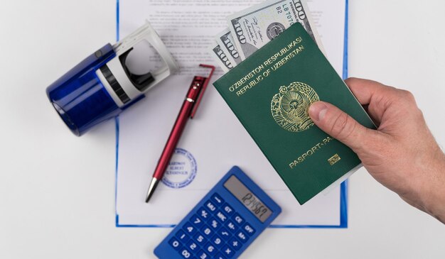 Hand holds out the passport of Uzbekistan with US dollars on the background of documents