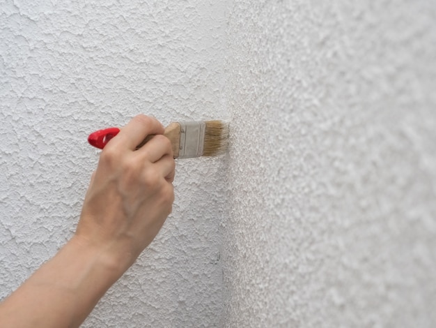 hand holds paint brush and painting a wall