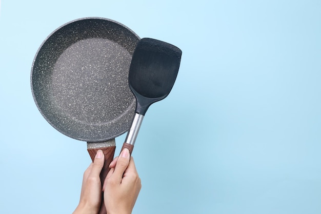 Hand holds pan and spatula isolated on blue background