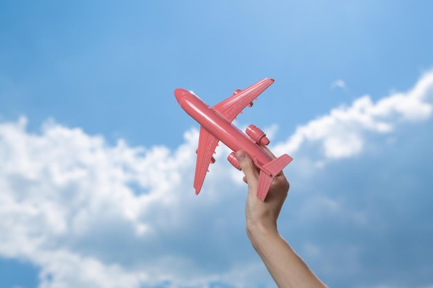 Hand holds pink model airplane on background of blue sky with clouds Travel concept