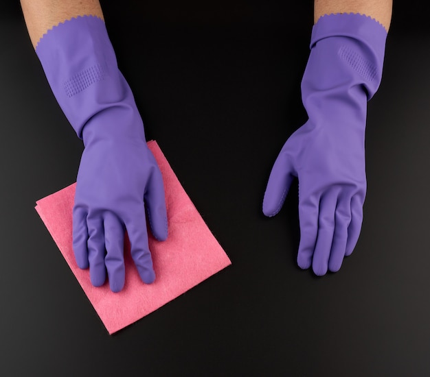 Photo hand holds a pink rag sponge for cleaning, protective purple rubber glove is worn on the arm