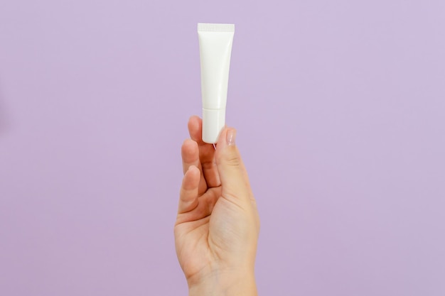 Hand holds plastic white tube isolated on lilac background Beauty concept Packaging tube for cosmetic products