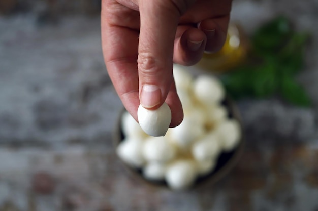 A hand holds a raw egg in front of a bowl of eggs.