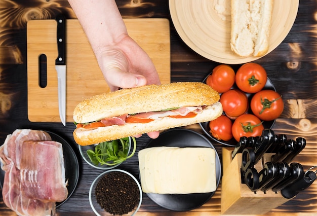 Hand holds a sandwitch over the kitchen table with ingredients