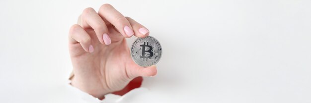 Hand holds silver bitcoin through hole in white paper