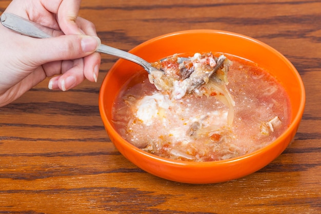 Hand holds tablespoon with cabbage soup over bowl