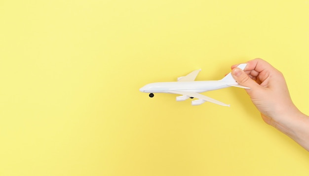Фото Рука держит игрушечный самолетик на желтом фоне. концепция летних каникул, путешествия. малыш веселится на летних каникулах. копировать пространство ..
