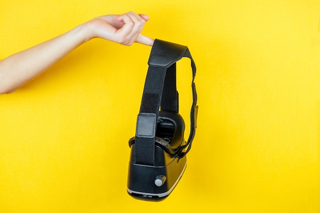 Hand holds a virtual reality helmet ( glasses ) on a yellow background