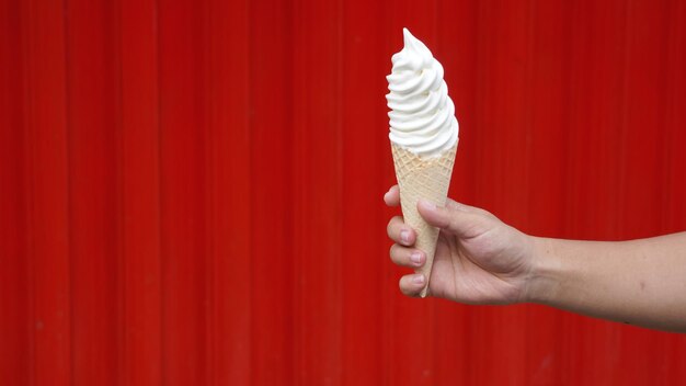 A hand holds a waffle cone with a red background.