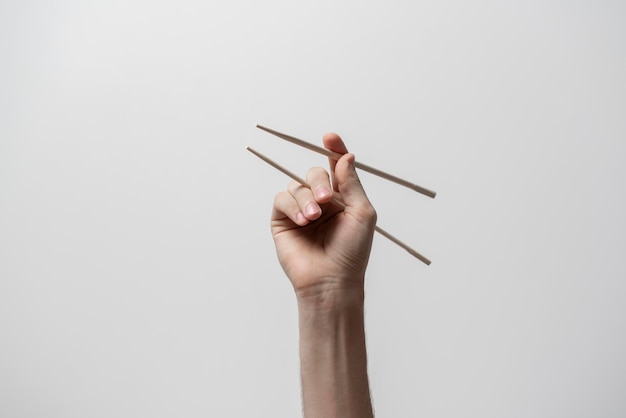 A hand holds wooden asian food chopsticks