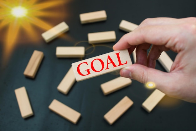 A hand holds a wooden block with the word goal on it.