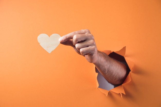 Hand holds a wooden heart on an orange background