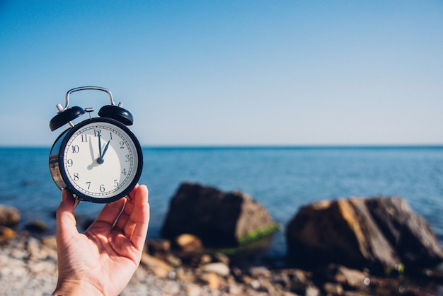 Hand houden horloge op strand achtergrond. Wekker op zee en zand achtergrond verschillende tijd met zomervakantie. Vakantie tijd concept.