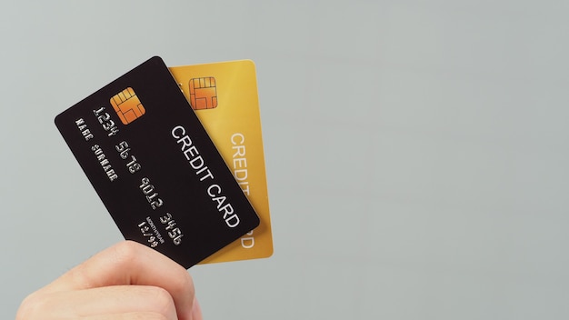 Hand houdt creditcard twee in zwarte en gouden kleur geïsoleerd op een grijze achtergrond.