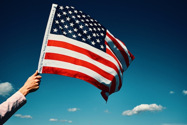 Hand houdt de nationale vlag van de VS tegen blauwe bewolkte hemel
