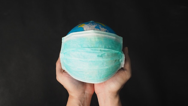 Hand houdt earth globe en gezichtsmasker op zwart background.covid-19 concept.