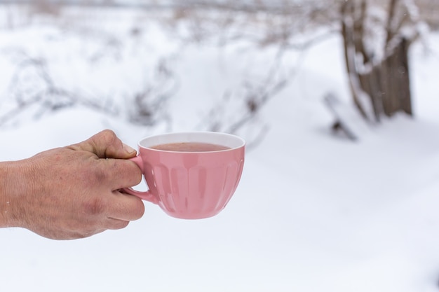 Hand houdt een roze mok met een drankje op een achtergrond van een winterlandschap