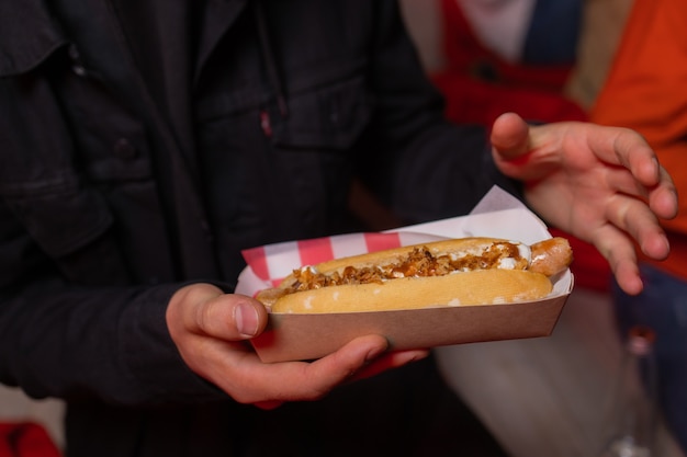 Hand houdt gebakken worst in deeg met ketchup in papieren rode witte verpakking op straat