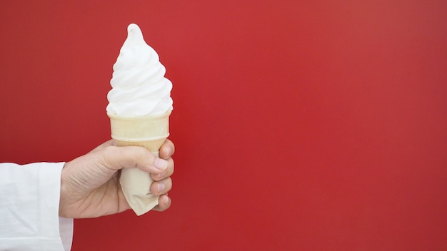 Hand houdt ijsje met rode achtergrond.