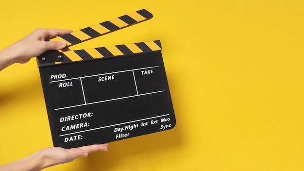Hand houdt klepel bord of Filmklapper of film leisteen. Het wordt gebruikt in filmproductie en bioscoop, filmindustrie op gele achtergrond.